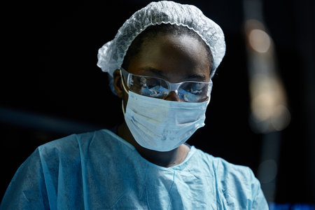 Dramatic low angle portrait of young African American woman as surgeon performing surgery in blue lights copy spaceの写真素材