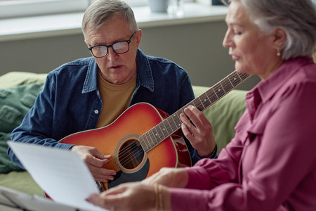 Portrait of senior man playing guitar and reading lyrics while singing song enjoying music at homeの写真素材
