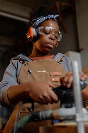Hispanic woman carefully handling woodworking tools in workshop, adjusting equipment for precision....