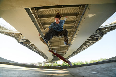 Skateboarder performing trick under large overhead bridge showing skill and agility mid-air with the...