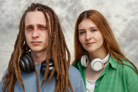 Portrait of two young people with long hair, one with dreadlocks, both wearing casual clothing and smiling while looking at camera, each wearing headphones around neckの写真素材