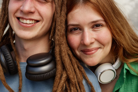 Young adults with differing hairstyles, smiling closely together while wearing large headphones. Displaying cheerful camaraderie and friendship in close-up photographの写真素材