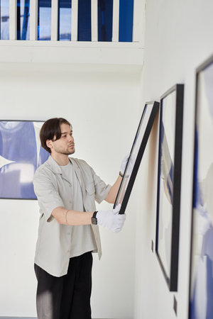 Minimal vertical portrait of Asian man hanging abstract pictures on wall while planning modern art gallery exhibitionの写真素材