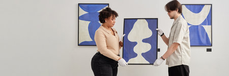 Header image of two people holding abstract painting while planning exhibition in modern art museum on white background copy spaceの写真素材