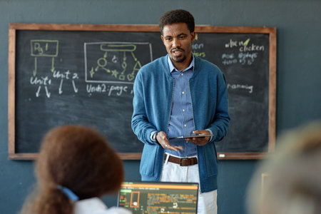Waist up portrait of young African American man as teacher explaining IT programming to children in...