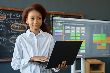 Waist up portrait of smiling African American teenage girl holding laptop while giving presentation on IT and programming in school classroom copy spaceの写真素材
