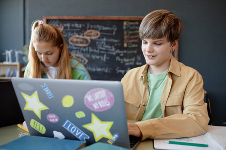 Portrait of smiling teenage boy using laptop with colorful stickers while enjoying lesson in school classroomの写真素材