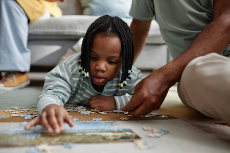 Young child laying pieces of puzzle on table with assistance from parent, creating an educational and bonding experience in a cozy indoor settingの写真素材