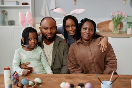 Family enjoying Easter celebration wearing bunny ears while painting eggs in kitchen setting with flowers in backgroundの写真素材