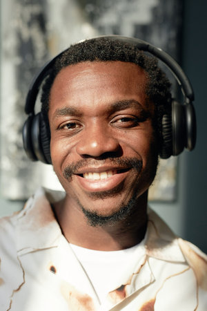Vertical closeup portrait of African American man wearing big headphones and smiling happily at...