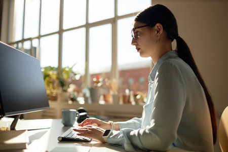 Side view portrait of successful young businesswoman using computer and looking at screen while...