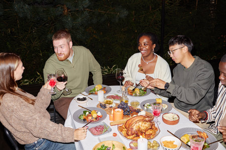 Multiethnic group of adults enjoying dinner party outdoors and celebrating holidays together, shot with flashの写真素材
