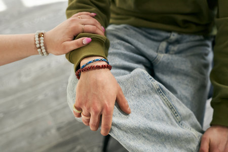 Close-up of two individuals hands, showing bracelets and casual arm placement. The jeans and green sweater create a relaxed atmosphereの写真素材