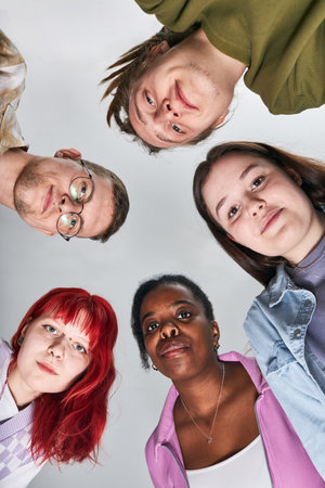 Portrait of diverse group of young adults looking up towards camera smiling in casual clothing...