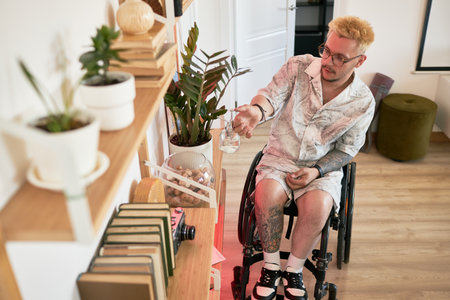 Caucasian man in wheelchair reaching for an item on a wooden shelf with plants around. Wearing...
