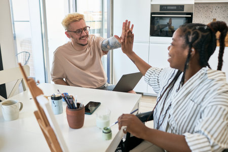 Two coworkers high-fiving each other in bright office environment. Smiling and looking happy,...