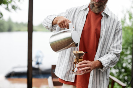 Cropped shot of bearded man making fresh pour over coffee standing outdoors in sunlight nature setting copy spaceの写真素材