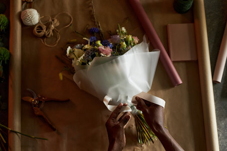Minimal top view of male hands tying ribbon on beautiful flower bouquet with craft paper background copy spaceの写真素材