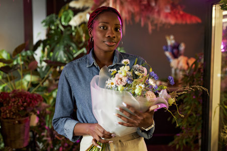 Waist up portrait of young African American woman holding beautiful bouquet posing in flower shop and looking at camera, copy spaceの写真素材