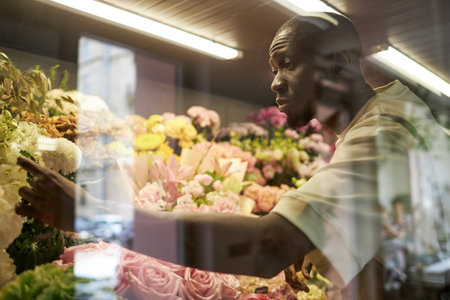 Side view portrait of young African American man caring for blooming flowers behind glass wall in flower store, copy spaceの写真素材