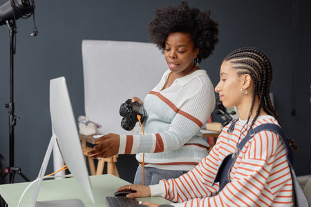 Side view portrait of two African American young women as female photographers collaborating in photo studio and looking at pictures on computer screenの写真素材