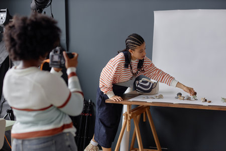 Portrait of Black young woman with braided hair as photographers assistant setting up for product photoshoot in studio copy spaceの写真素材