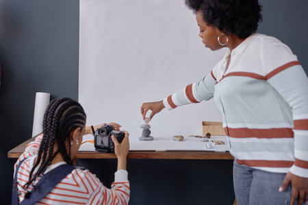 Minimal back view of two African American woman as photographers working together in studio while working with natural stones in product photography set copy spaceの写真素材