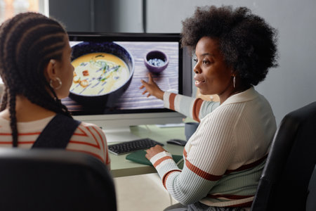 Side view portrait of creative young Black woman discussion photos with friend or colleague and...