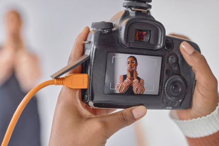Close up of photographer holding camera with portrait of Black young woman on screen during photoshoot in studio, copy spaceの写真素材