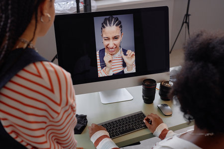 Over shoulder view at two women looking at portrait pictures on computer screen during photo...