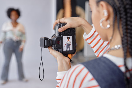 Closeup of young Black woman as female photographer holding camera while taking pictures of model in...