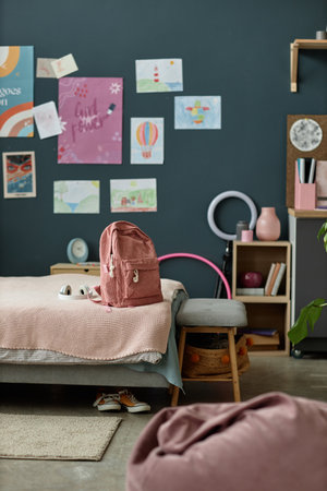 Cozy kids bedroom with a study area featuring a backpack on gray sofa, posters displaying fun artwork on dark wall, and neatly arranged storage for a tidy organized spaceの写真素材