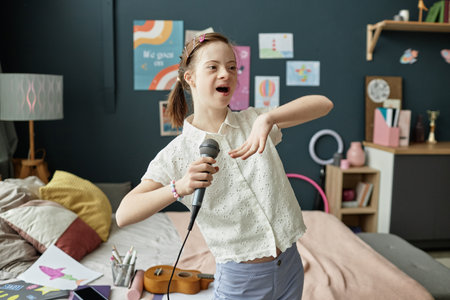 Joyful girl holding microphone and singing in her bedroom filled with art posters and scattered books, portraying an energetic and lively atmosphereの写真素材