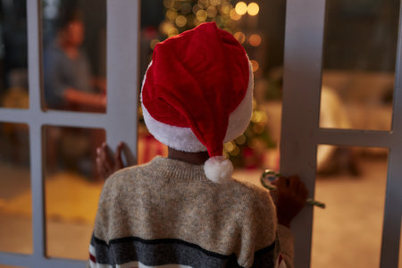 Back view of curious little boy wearing Christmas hat opening doors sneaking into living room to catch Santa Claus copy spaceの写真素材