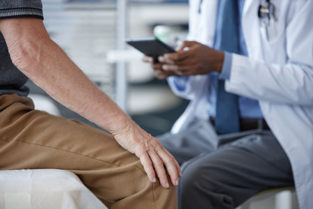 Side view closeup of unrecognizable senior patient siting on examination table in clinic with doctor...