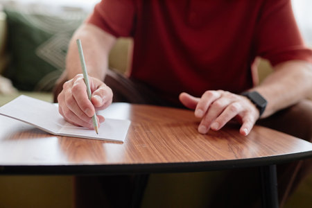 Close up of senior man writing music or poetry at home with focus on hands tapping table in...