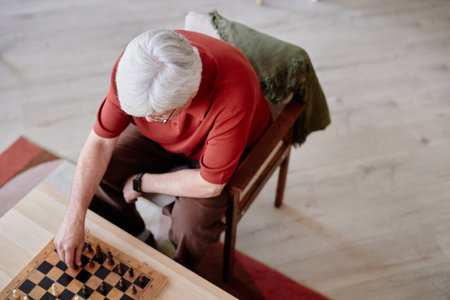 Top view of white haired senior man playing chess solo minimal shot with red color accents copy...