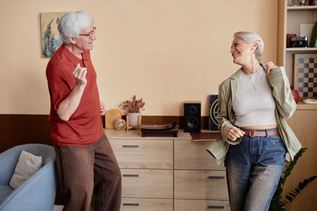 Side view portrait of two modern senior people dancing joyfully together listening to music at home...