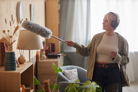 Side view portrait of modern mature woman enjoying cleaning at home and listening to music while...