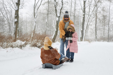 Full length authentic scene of happy family enjoying sledding in winter forestの写真素材
