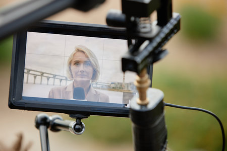 Close up of woman's face on digital screen of professional video camera recording news outdoors,...