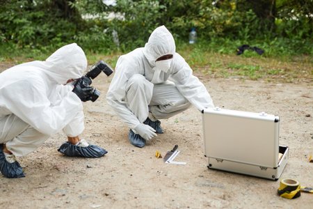 Two people wearing protective suits working at crime scene taking photographs and gathering...