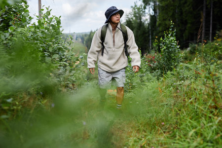 Full length portrait of Asian man backpacking in forest and walking towards camera on forest trail...