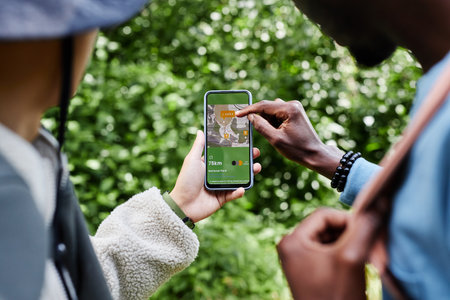 Over shoulder view of two tourists using navigation app with map and pointing at smartphone screen...