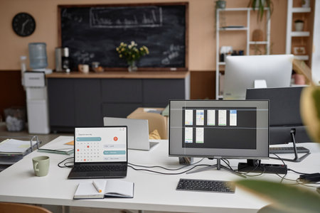 Modern office desk setup equipped with laptop displaying page of calendar and computer with app...