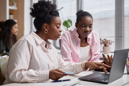 Medium shot of two African American women emotionally discussing business issues pointing at laptop...