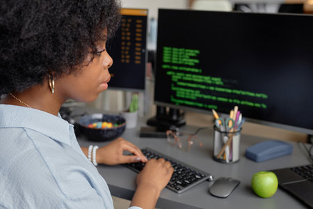 Side view of young African American software developer typing on keyboard while writing code for...