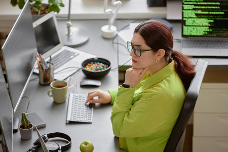High-angle side view shot of young red-haired female software engineer wearing green shirt and...