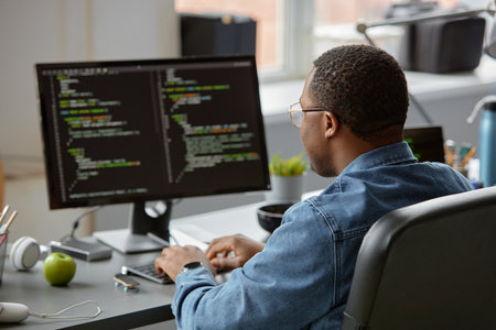Back view of male African American IT specialist in glasses code programming on computer while...