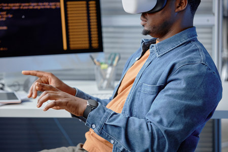 Cropped side view of concentrated male African American software engineer coding in headset using VR systems at office workplace, copy spaceの写真素材